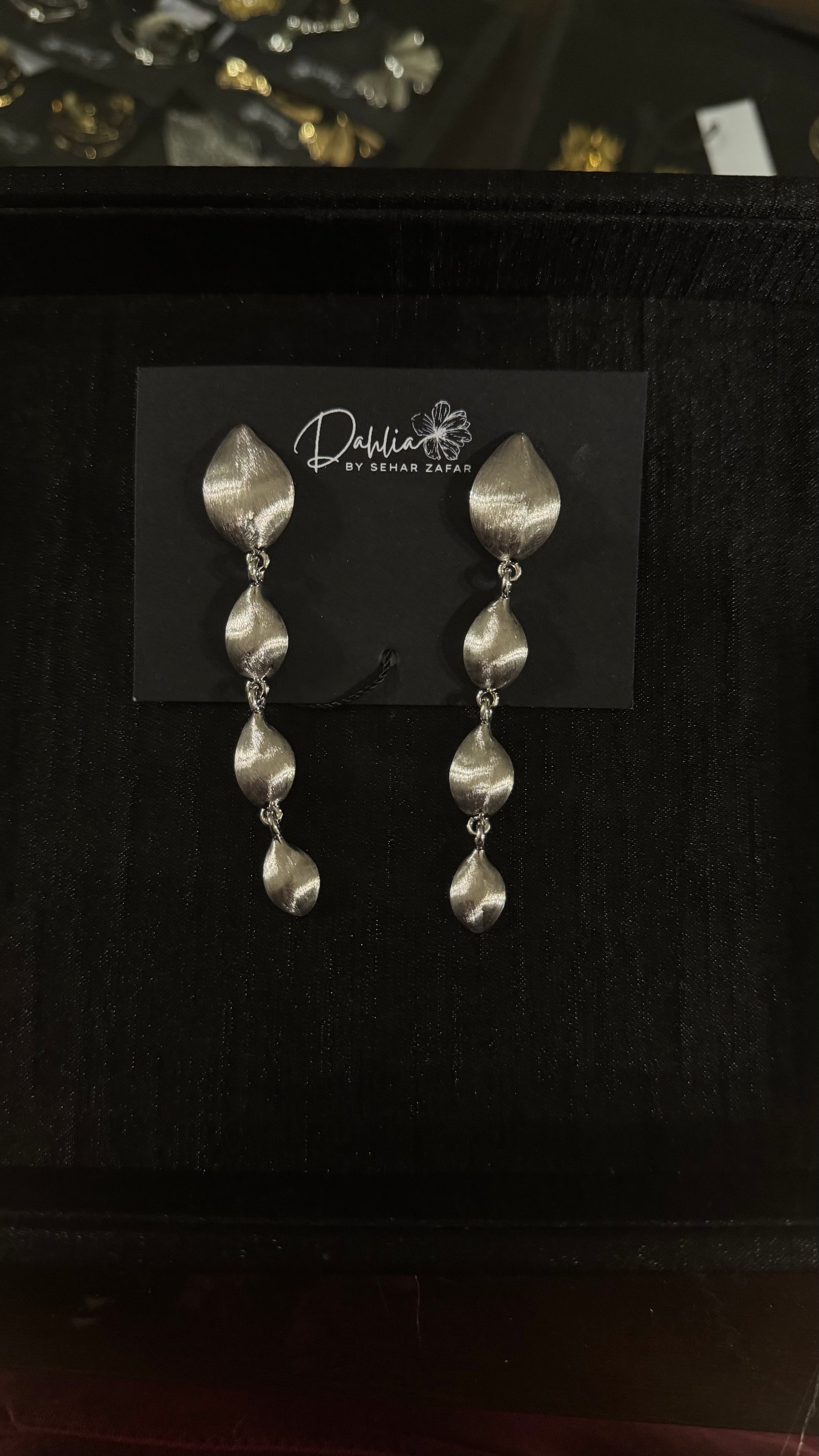 Gold cascading leaf earrings with textured metallic finish on black branded card