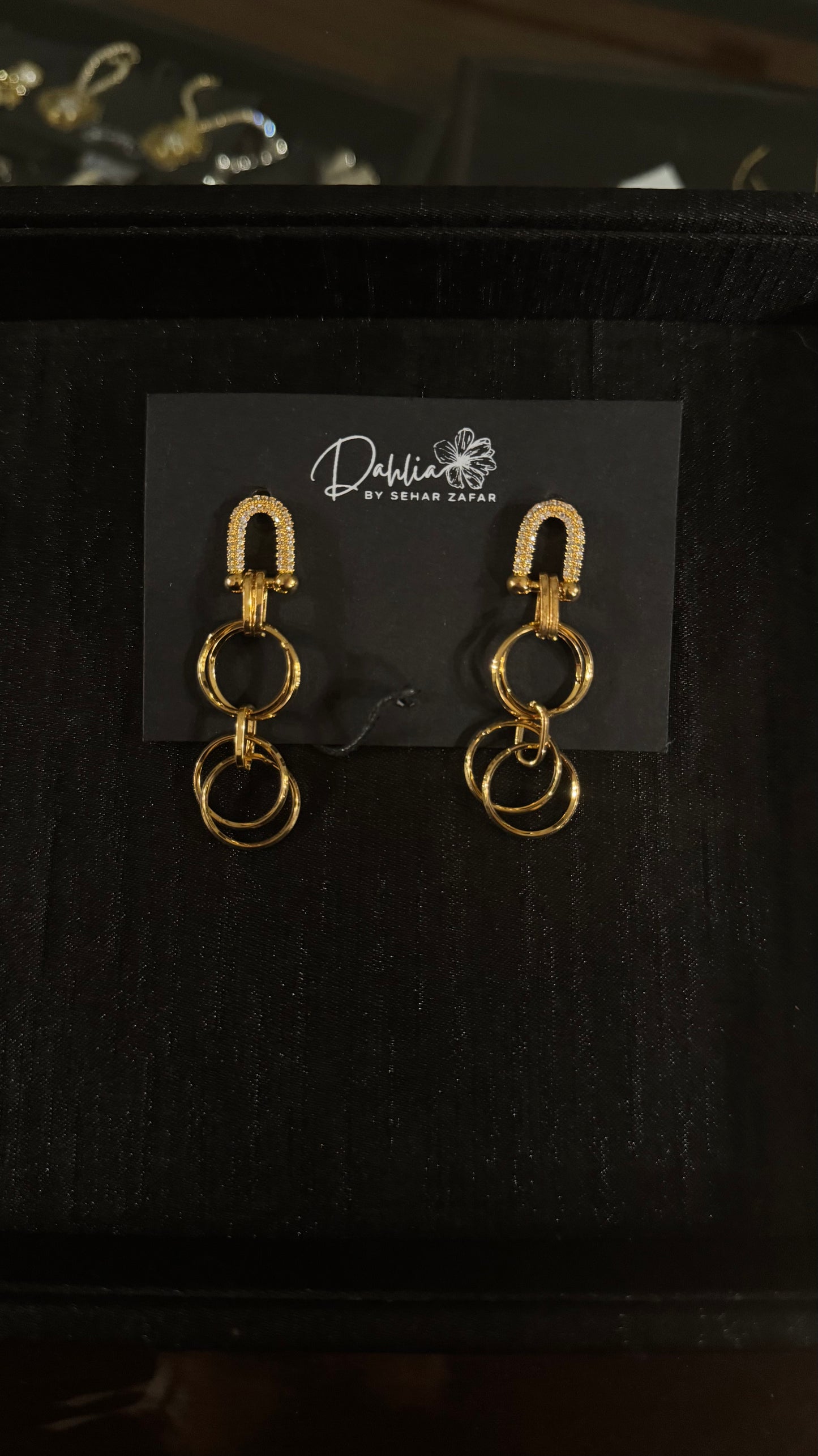 Gold U-shaped gem earrings with interlinked circular drops on black branded card