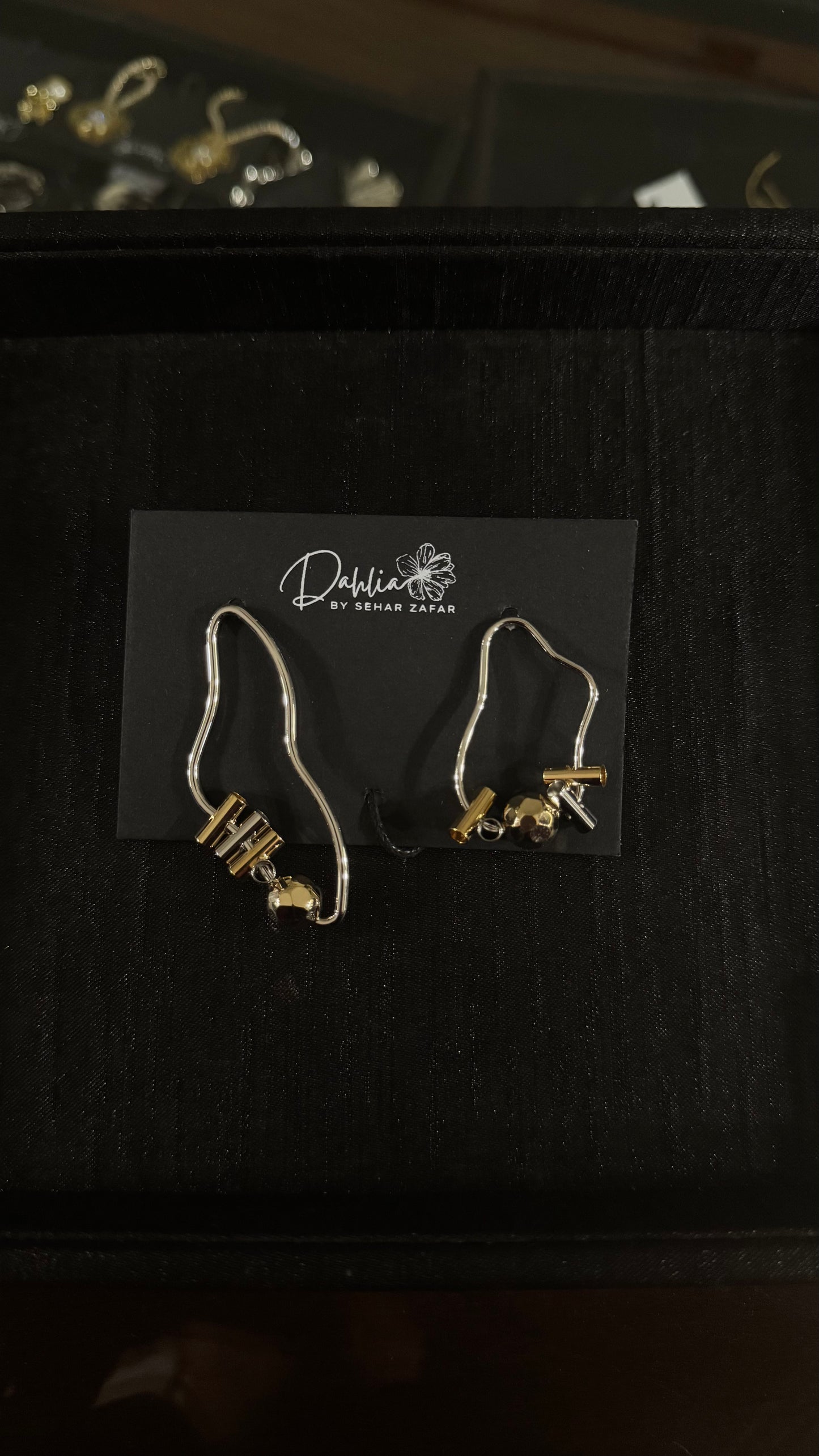 Abstract wire earrings with gold-toned beads and sculptural form on black branded card
