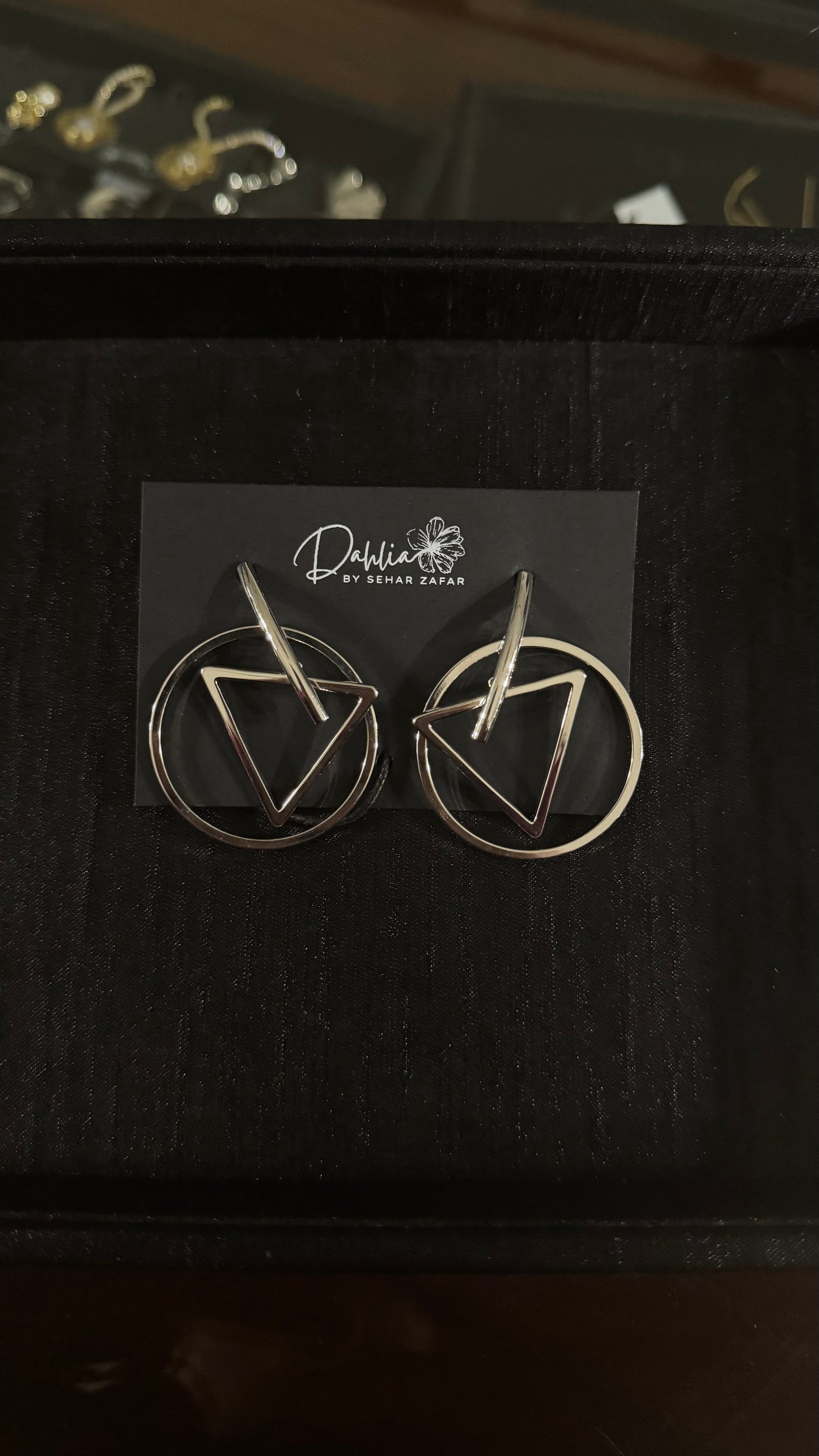Gold geometric earrings with triangle and circle frame design on black branded card