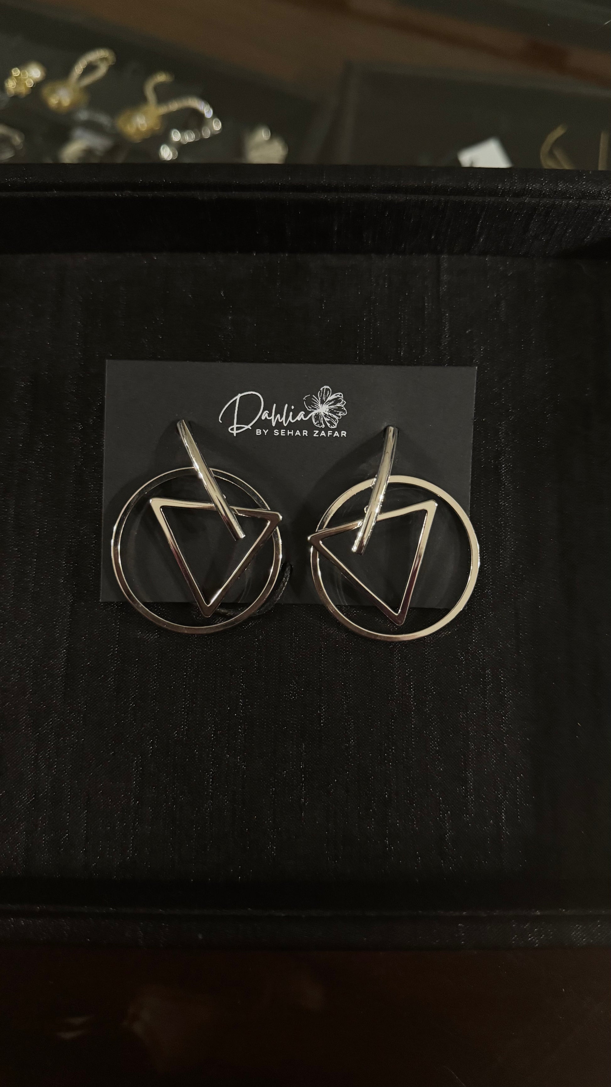 Gold geometric earrings with triangle and circle frame design on black branded card