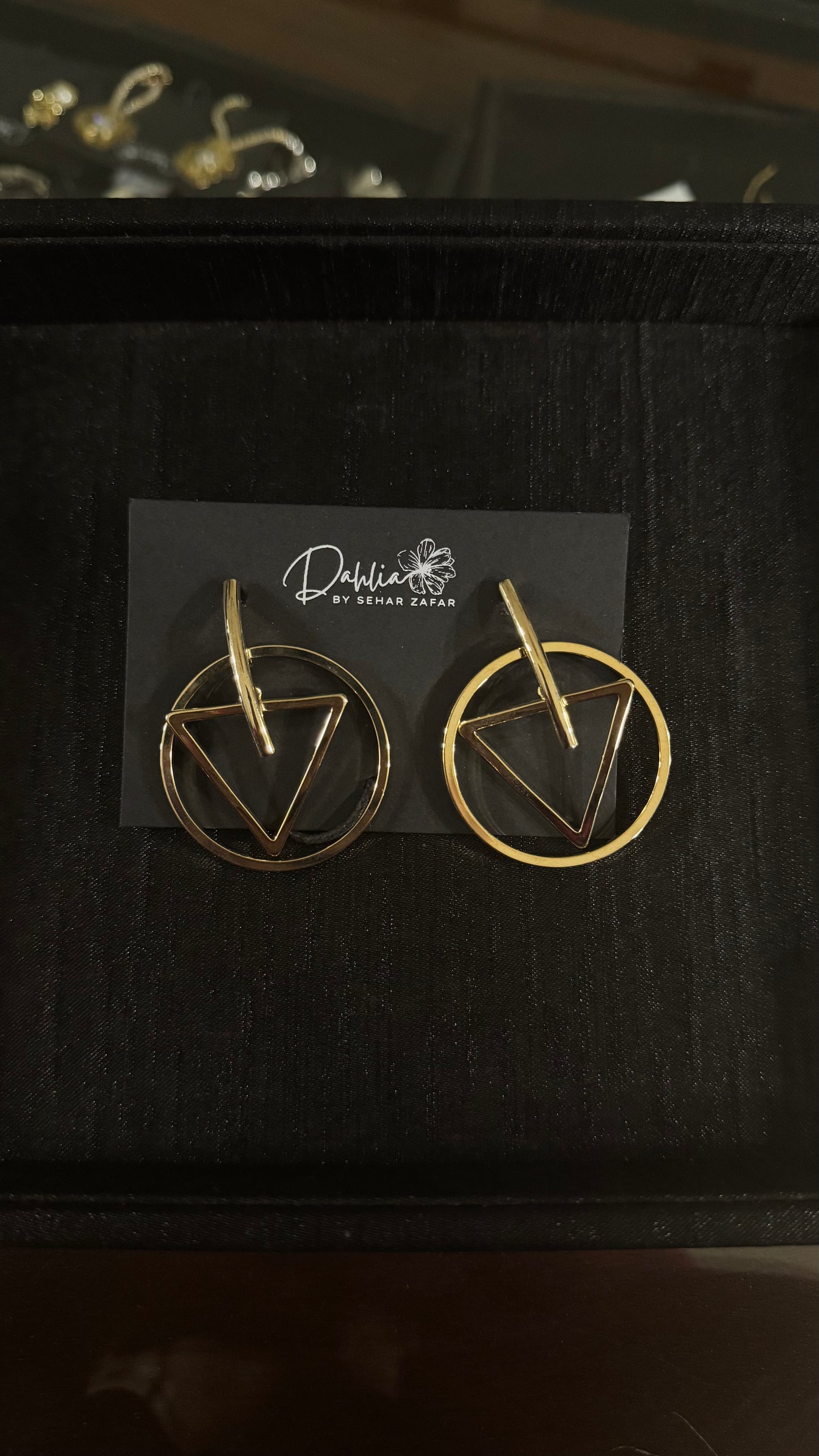 Gold geometric earrings with triangle and circle frame design on black branded card