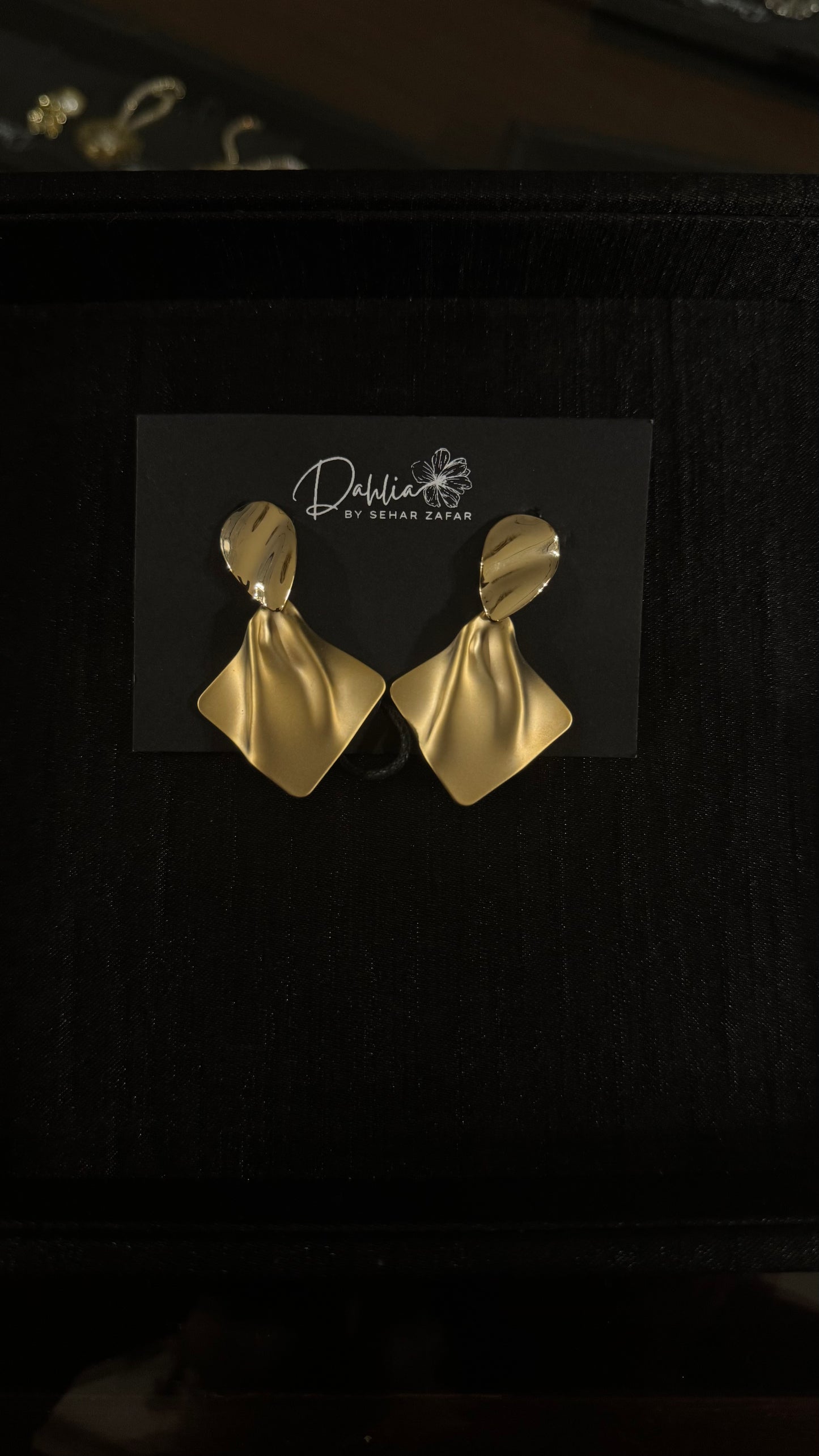 Gold sculptural petal earrings with diamond-shaped drop on black branded card