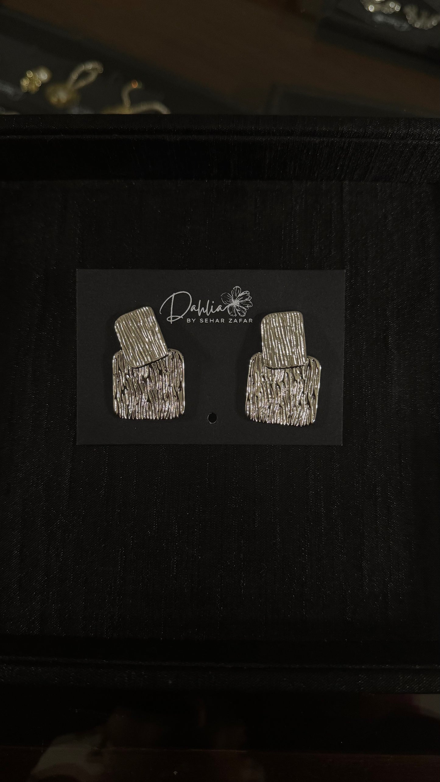 Gold textured rectangle earrings with geometric drop design on black branded card