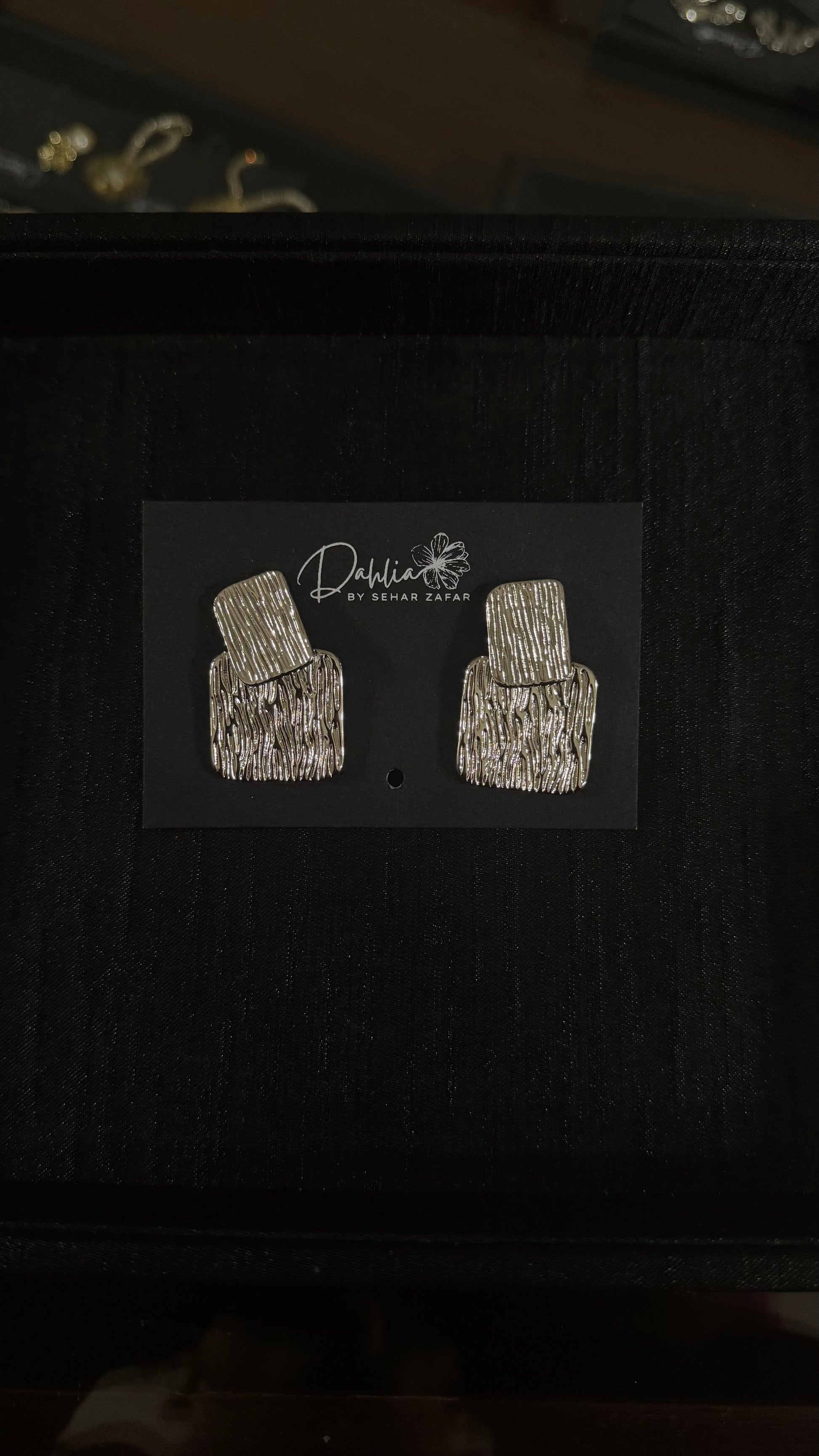 Gold textured rectangle earrings with geometric drop design on black branded card