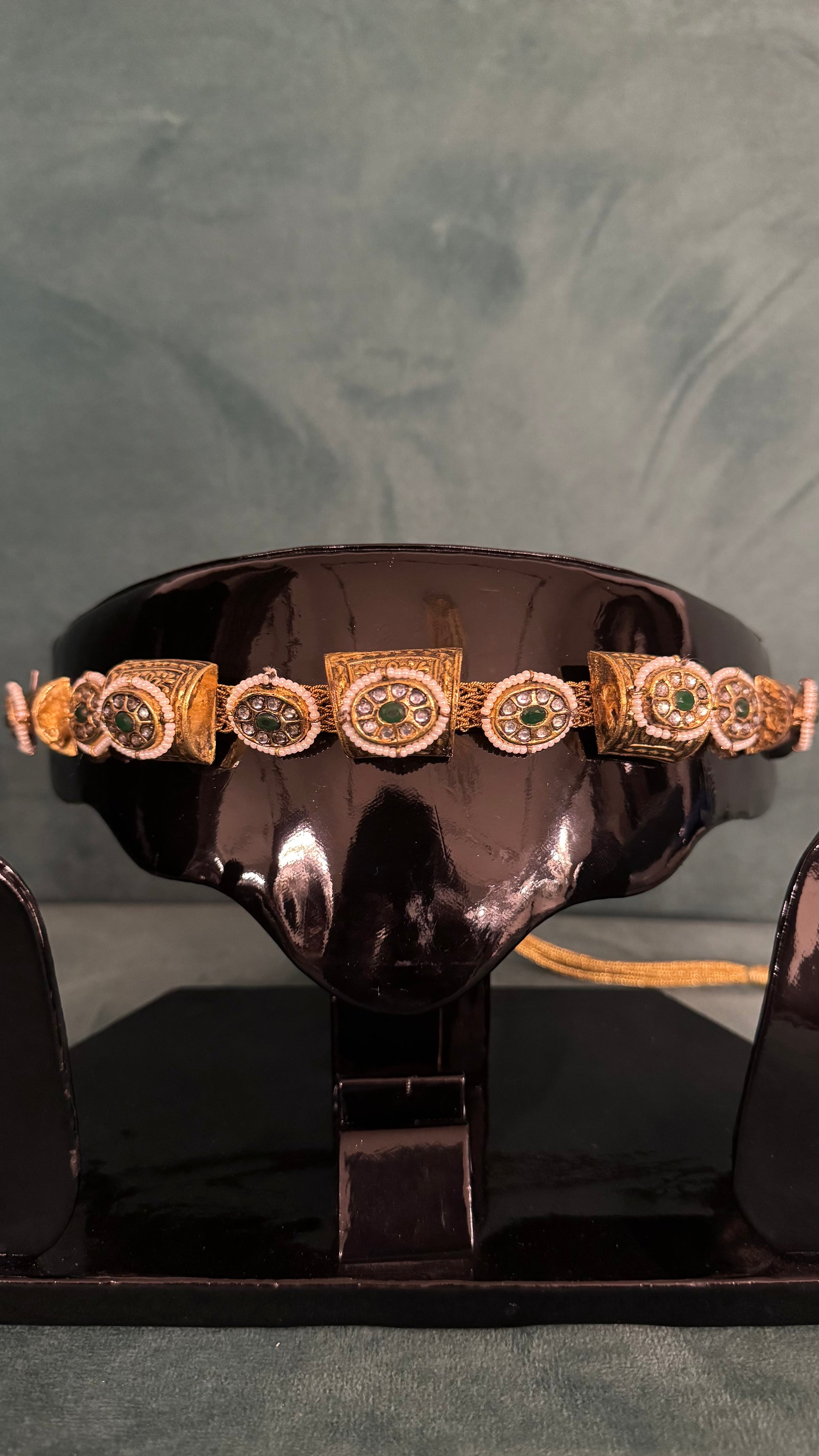 Gold choker necklace sets with green and white gemstone detailing on black display stand