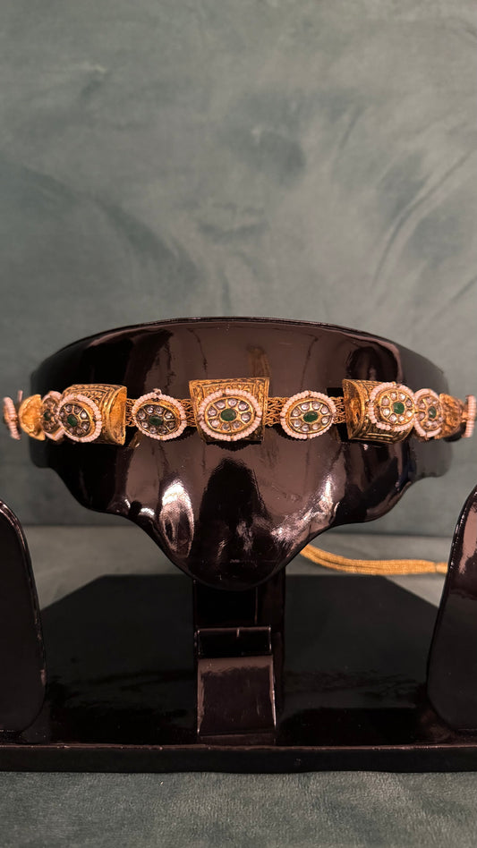 Gold choker necklace sets with green and white gemstone detailing on black display stand