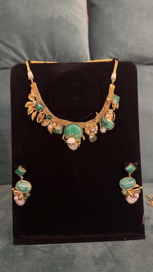 Traditional necklace sets with green gemstones, leaf motifs, and teardrop accents on black velvet stand