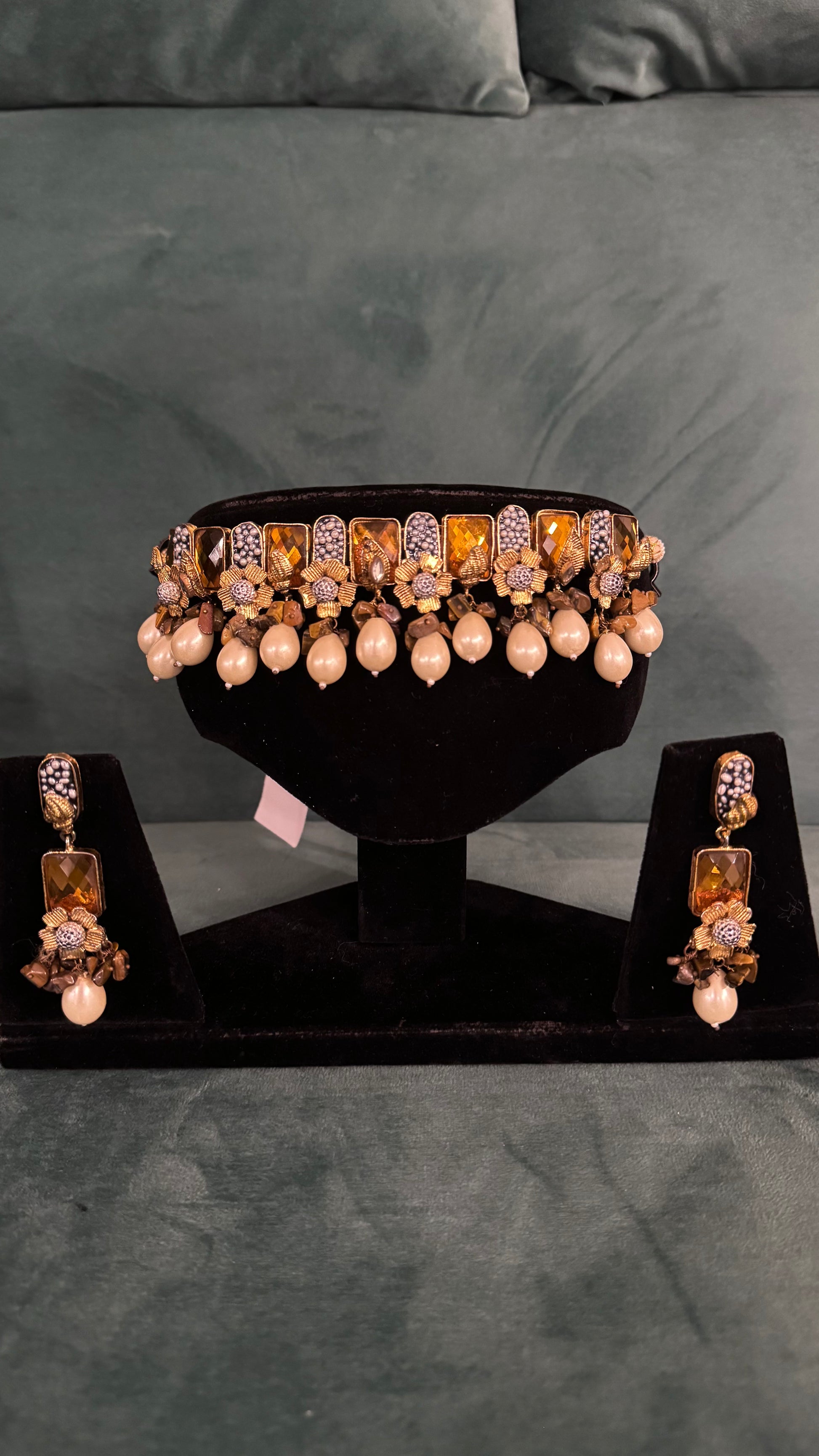 Traditional choker necklace sets with amber stones, floral motifs, and pearl drops on black velvet stand