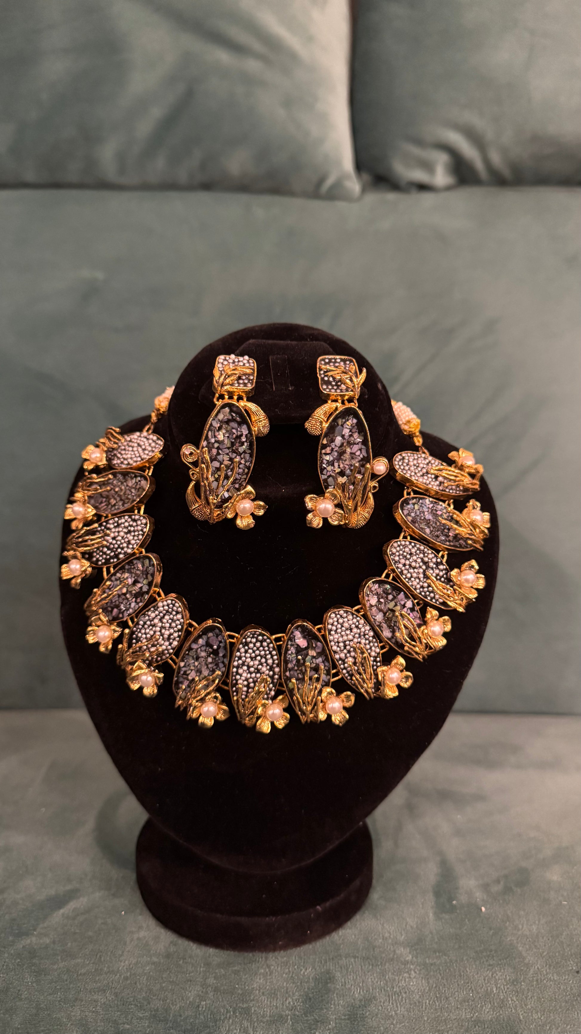 Traditional necklace sets with dark stones, floral motifs, and pearl accents on black velvet stand