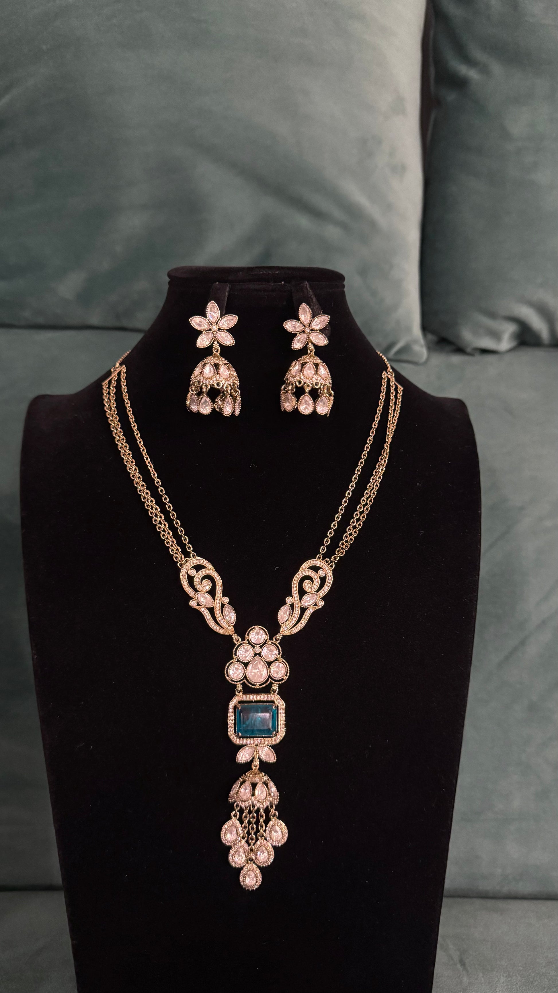 Elegant necklace sets with blue gemstone pendant, floral motifs, and gold chain on black velvet bust