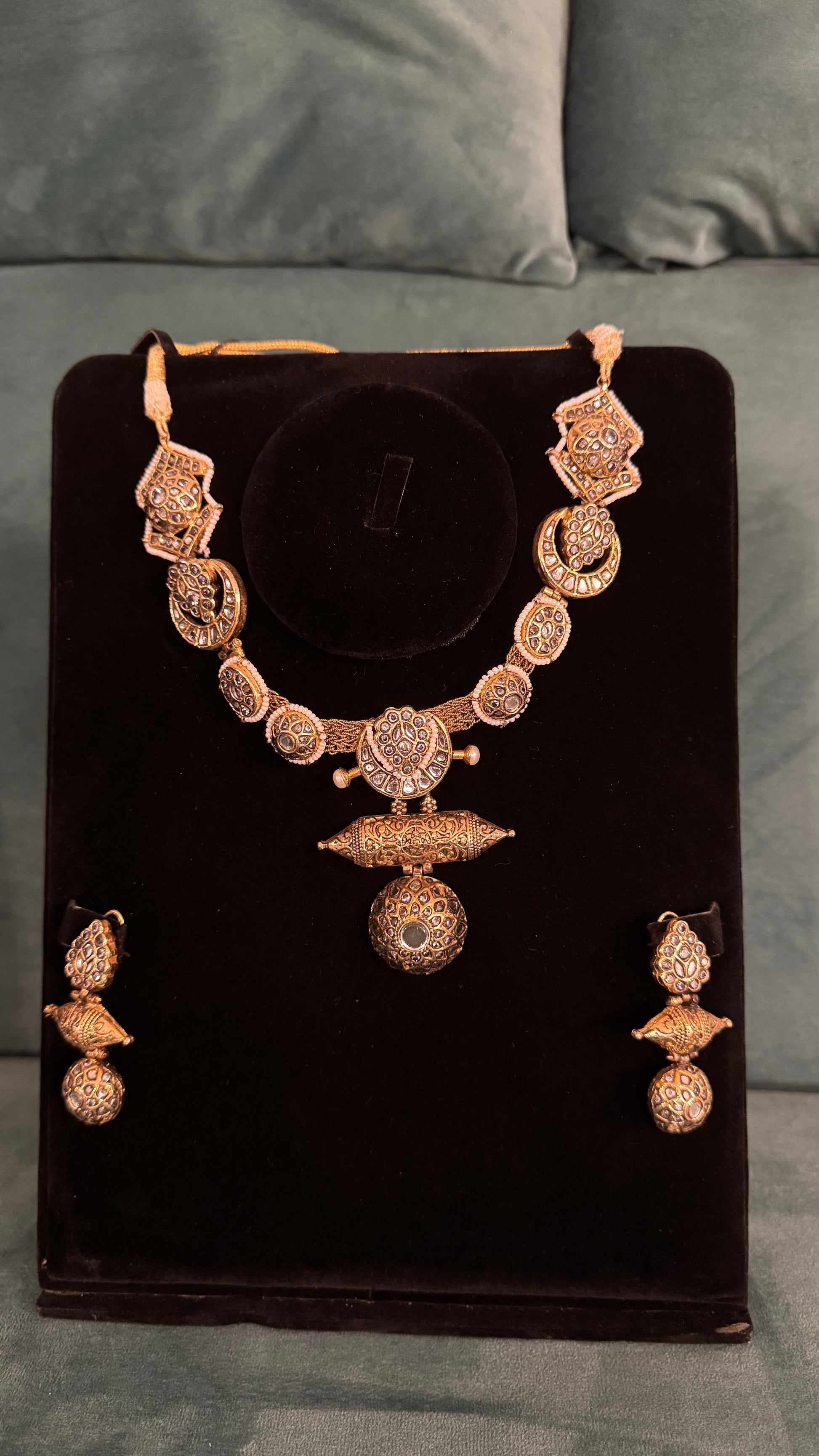 Traditional necklace sets with ornate gold filigree, spherical pendants, and geometric motifs on black velvet stand