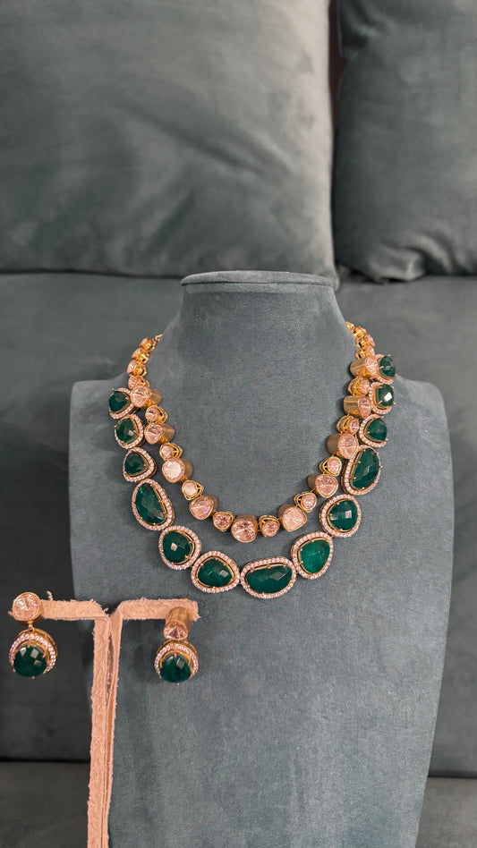Luxury necklace sets with green teardrop stones, clear faceted gems, and gold detailing on dark velvet stand