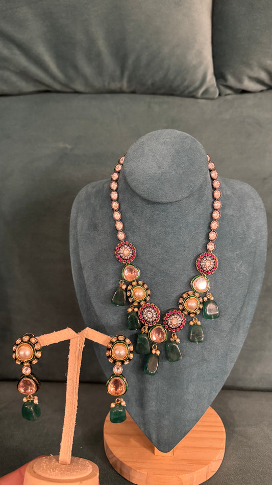 Traditional necklace sets with pink, white, and green stones and teardrop beads on velvet bust and wooden stand