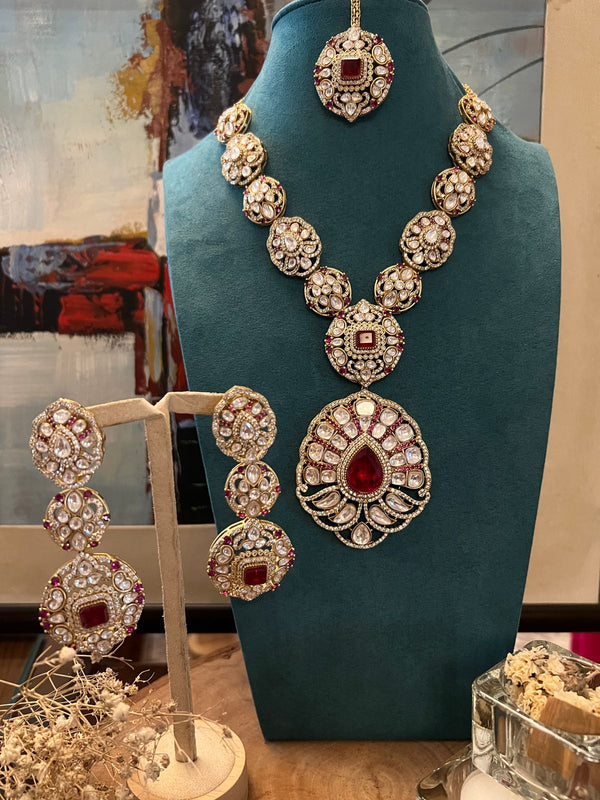 Kundan necklace set with ruby centerpiece and matching earrings displayed on a blue stand.
