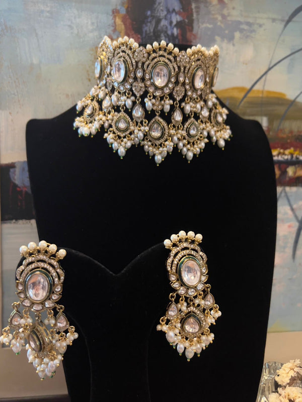Kundan choker necklace with pearl detailing and matching earrings displayed on a black stand.