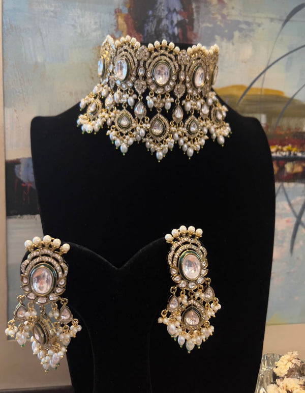 Kundan choker necklace with pearl detailing and matching earrings displayed on a black stand.
