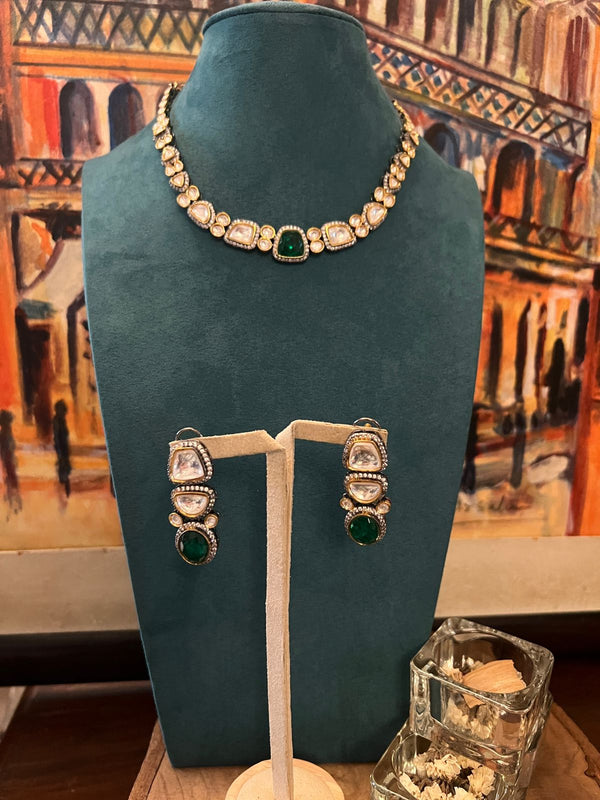Minimal Kundan necklace with emerald centerpiece and matching earrings on a teal stand.