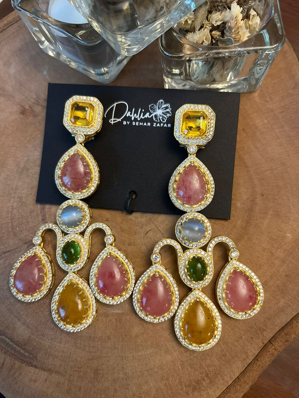 Premium gold plated earrings with multicolor stones including pink, yellow, and green, displayed on a wooden surface.