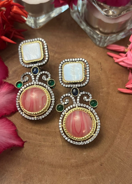 Pink doublet stone earrings with pearl tops, crystal framing, and green and blue accents displayed on a wooden surface with floral decor.