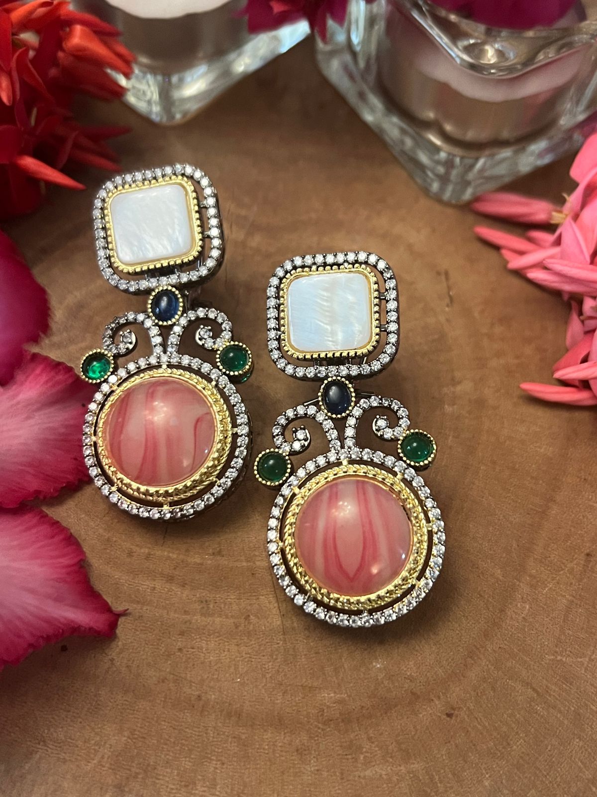 Pink doublet stone earrings with pearl tops, crystal framing, and green and blue accents displayed on a wooden surface with floral decor.