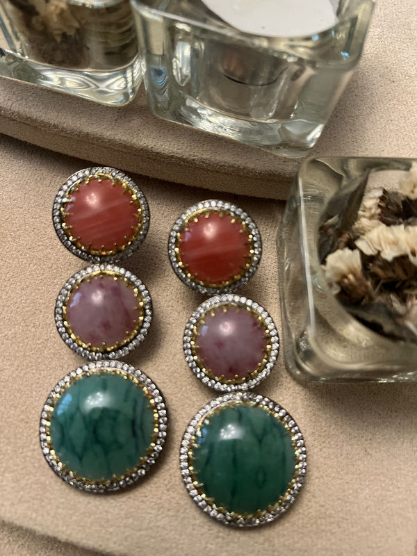 Triple stone drop earrings with red, lavender, and green doublet stones framed in crystals displayed on a soft fabric surface.