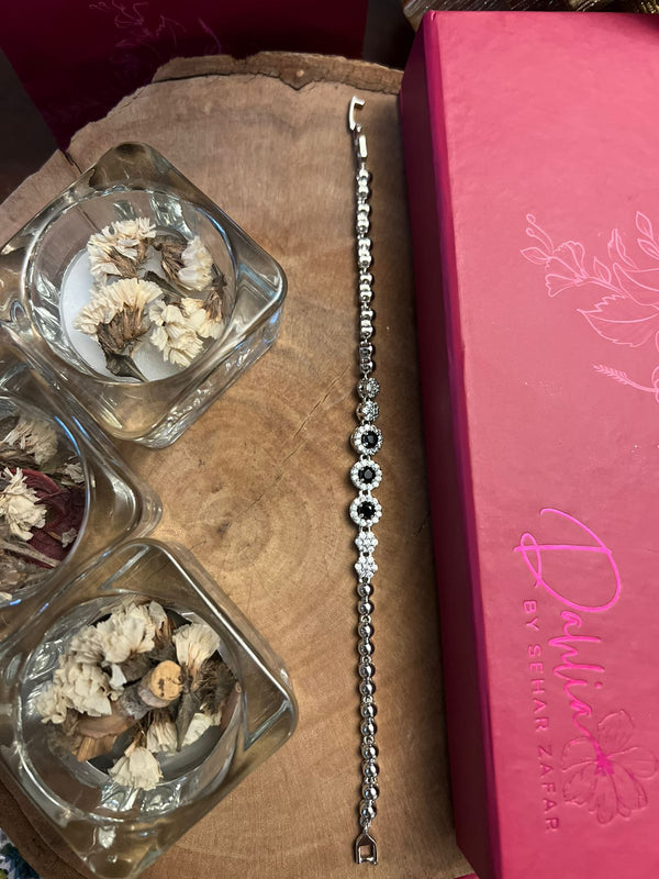 A bracelet with a rustic design, featuring silver accents and beads, displayed on a wooden table alongside a pink box with floral designs.