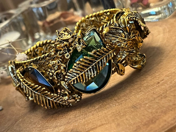 A gold-colored bracelet with a navy stone centerpiece and decorative leaf-like patterns, displayed on a wooden surface.