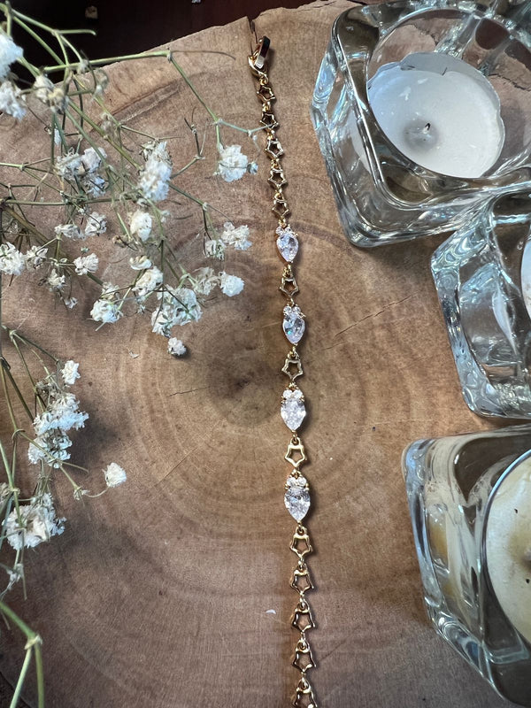 Gold bracelet with marquise-cut stones displayed on a wooden surface.