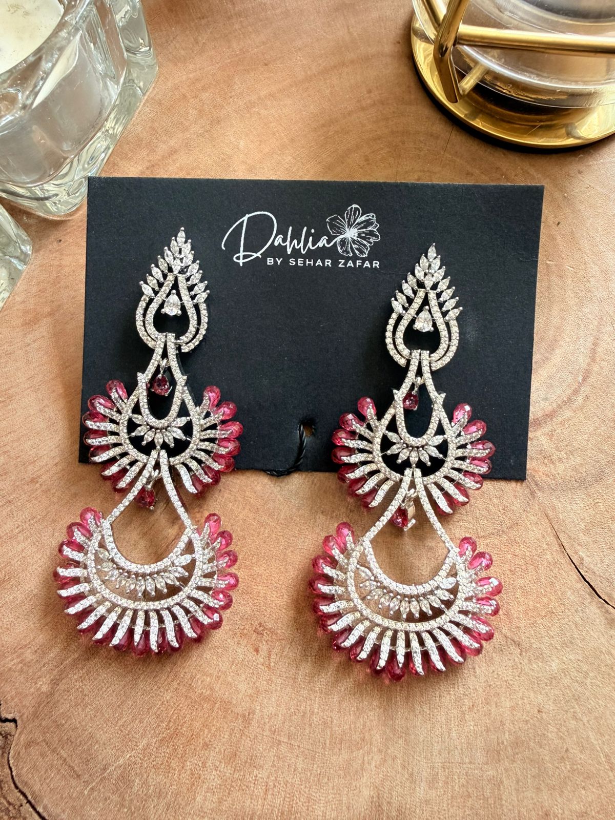Ornate earrings on a black card with 'Dahlia by Sehar Zafar' branding, placed on a wooden surface.