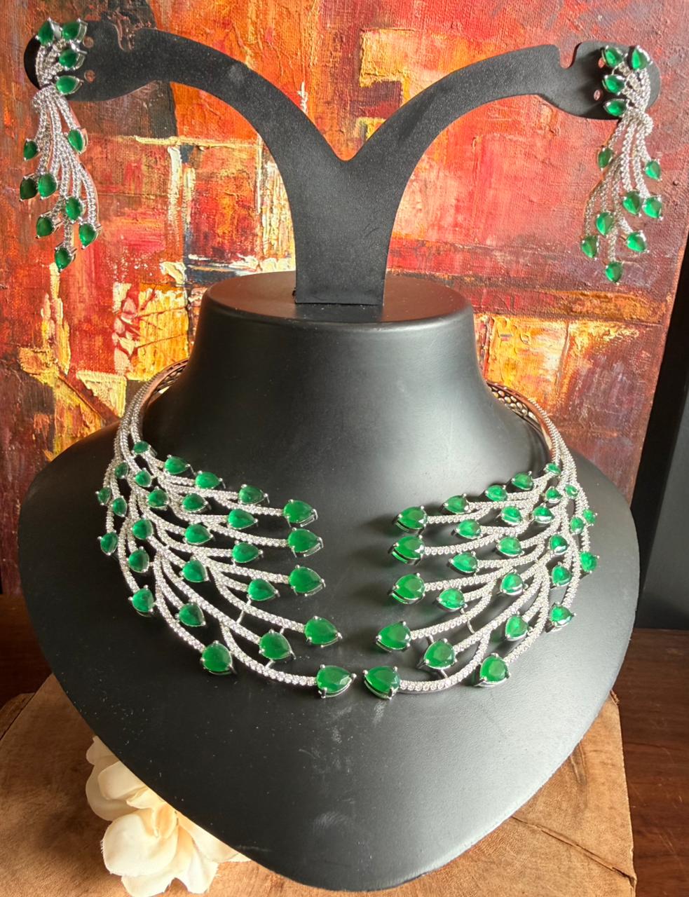 Green and silver necklace on a black mannequin bust with a colorful abstract background