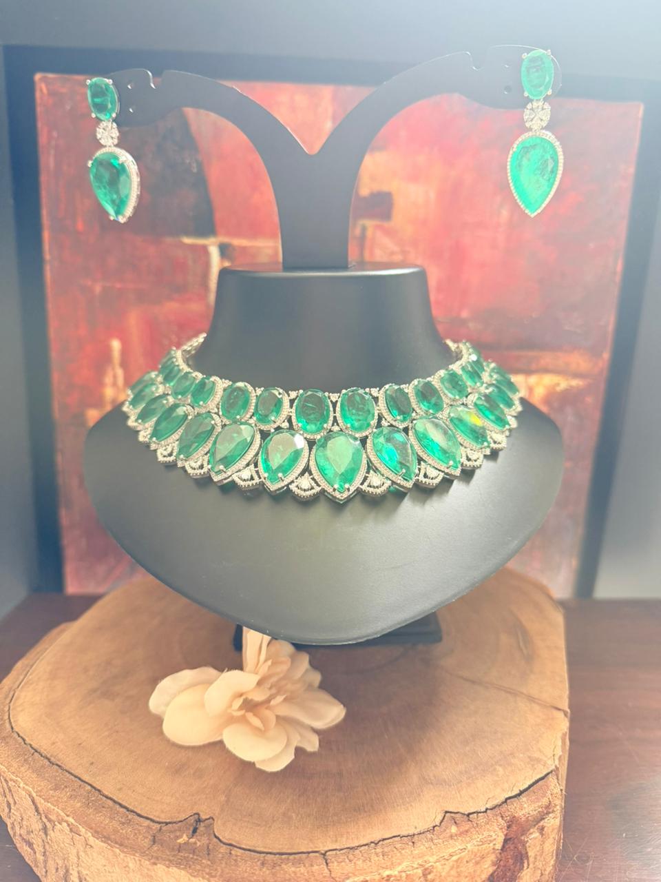 Green gemstone necklace and earrings on a black mannequin bust with a floral decoration.