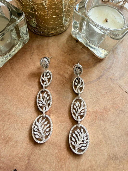 Silver leaf-shaped earrings on a wooden surface with candles in the background