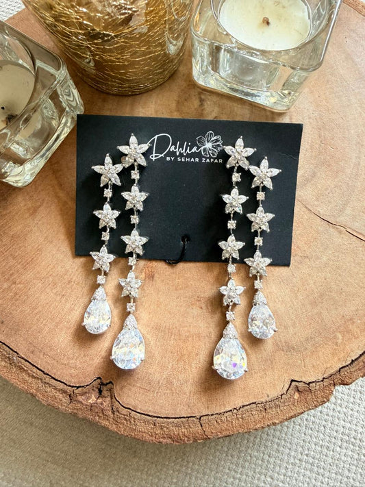 Star-shaped earrings on a black card with 'Dahlia' branding, placed on a wooden surface.