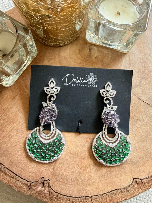 Green and silver earrings on a black card with 'Dahlia' branding, placed on a wooden surface.