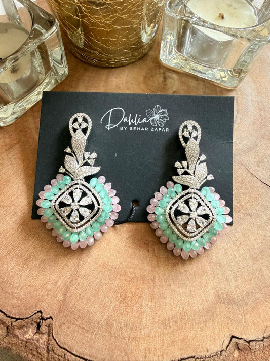 Decorative earrings on a black card with 'Dahlia by Sehar Zafar' branding, placed on a wooden surface.