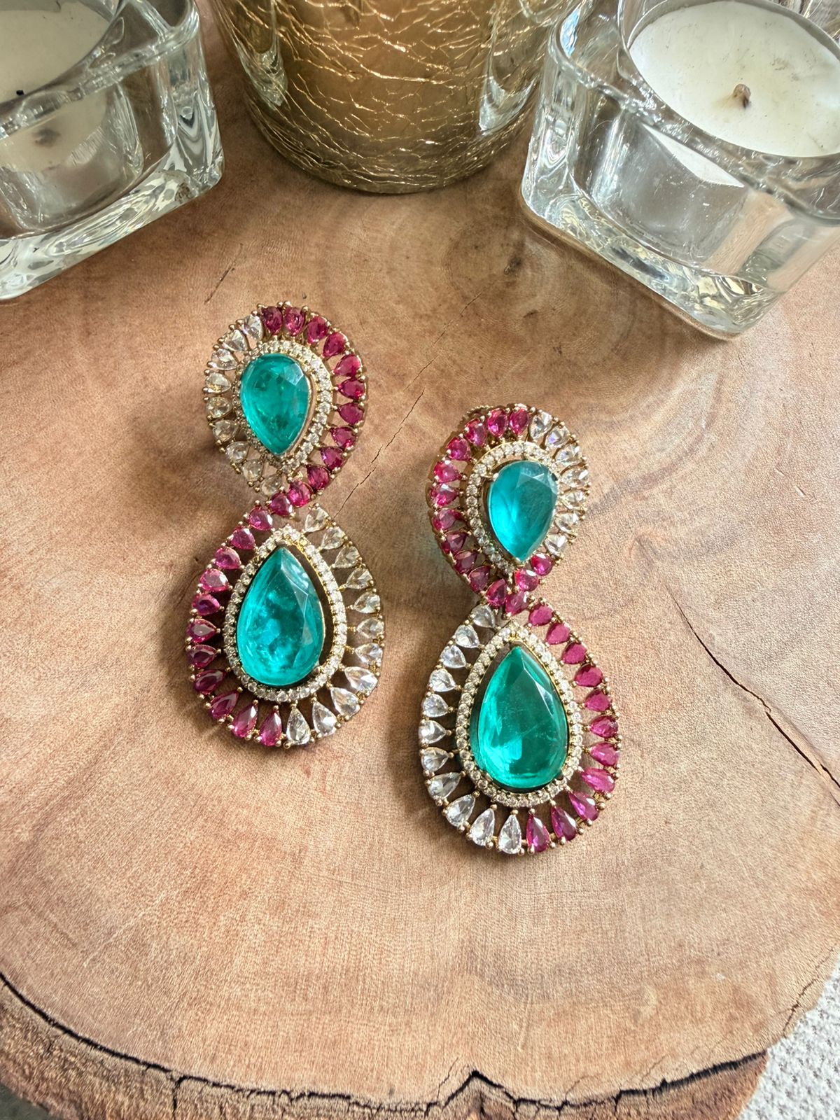 Pair of earrings with teal and pink gemstones on a wooden surface.