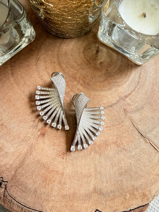 Silver fan-shaped earrings on a wooden surface with candles in the background