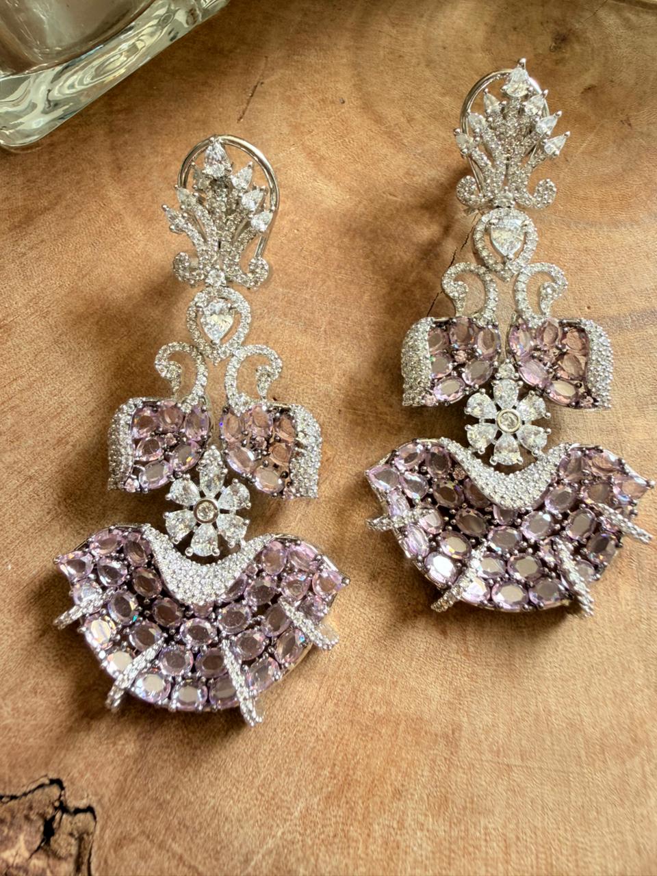 Blush pink crystal chandelier earrings with floral design and silver tone detailing on wooden surface