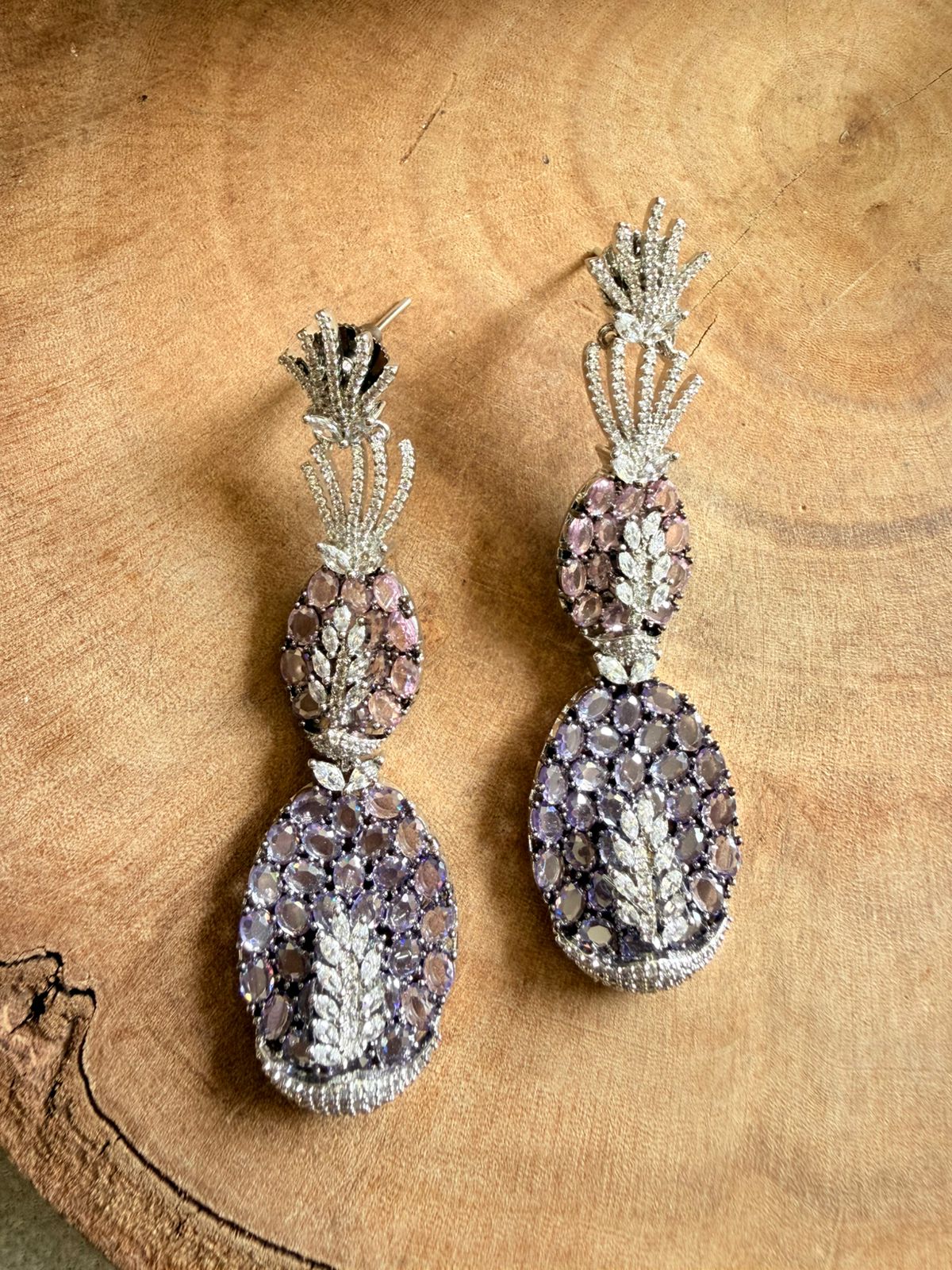 Pair of ornate earrings with purple and silver design on a wooden surface