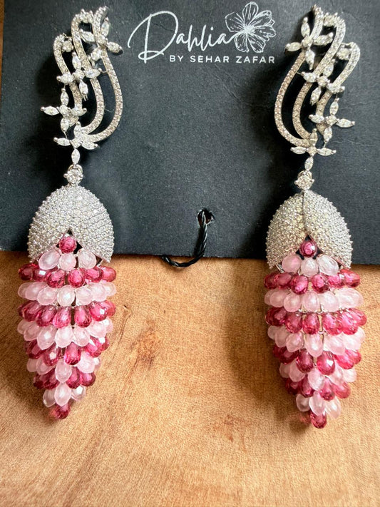 Pair of ornate earrings with pink and white beads on a wooden surface, branded 'Dahlia by Sehar Zafar'.