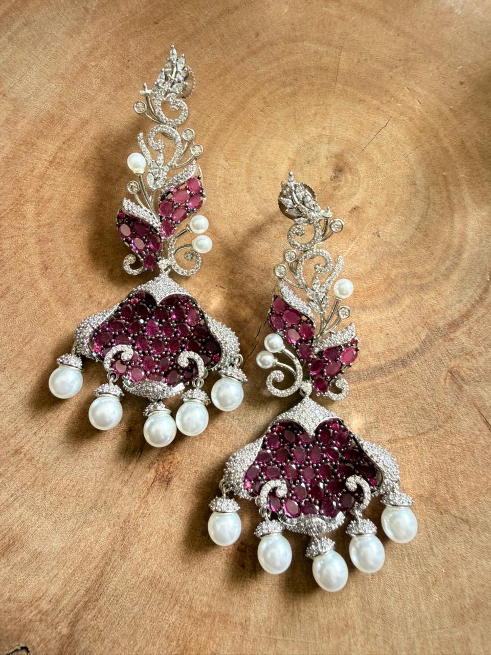 Ornate earrings with red gemstones and white pearls on a wooden surface