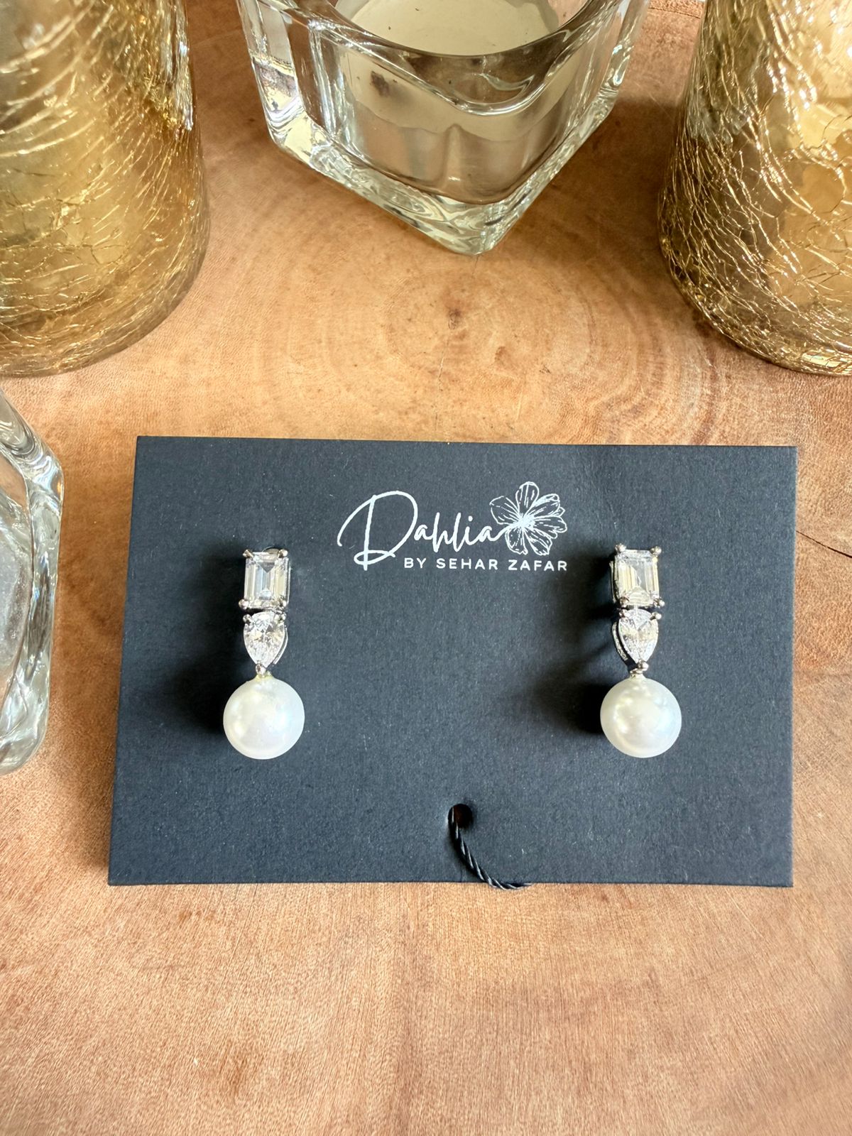 Pair of earrings on a display card with 'Dahlia by Sehar Zafar' branding on a wooden surface.