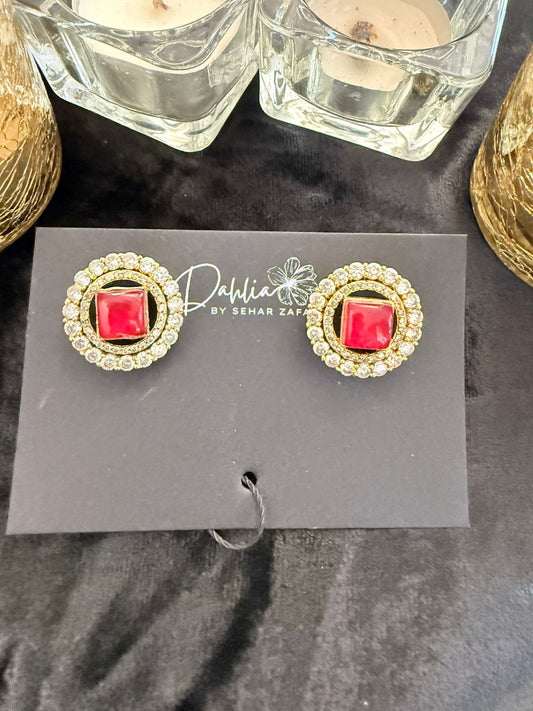 Gold earrings with red gemstones on a display card, placed on a dark surface.