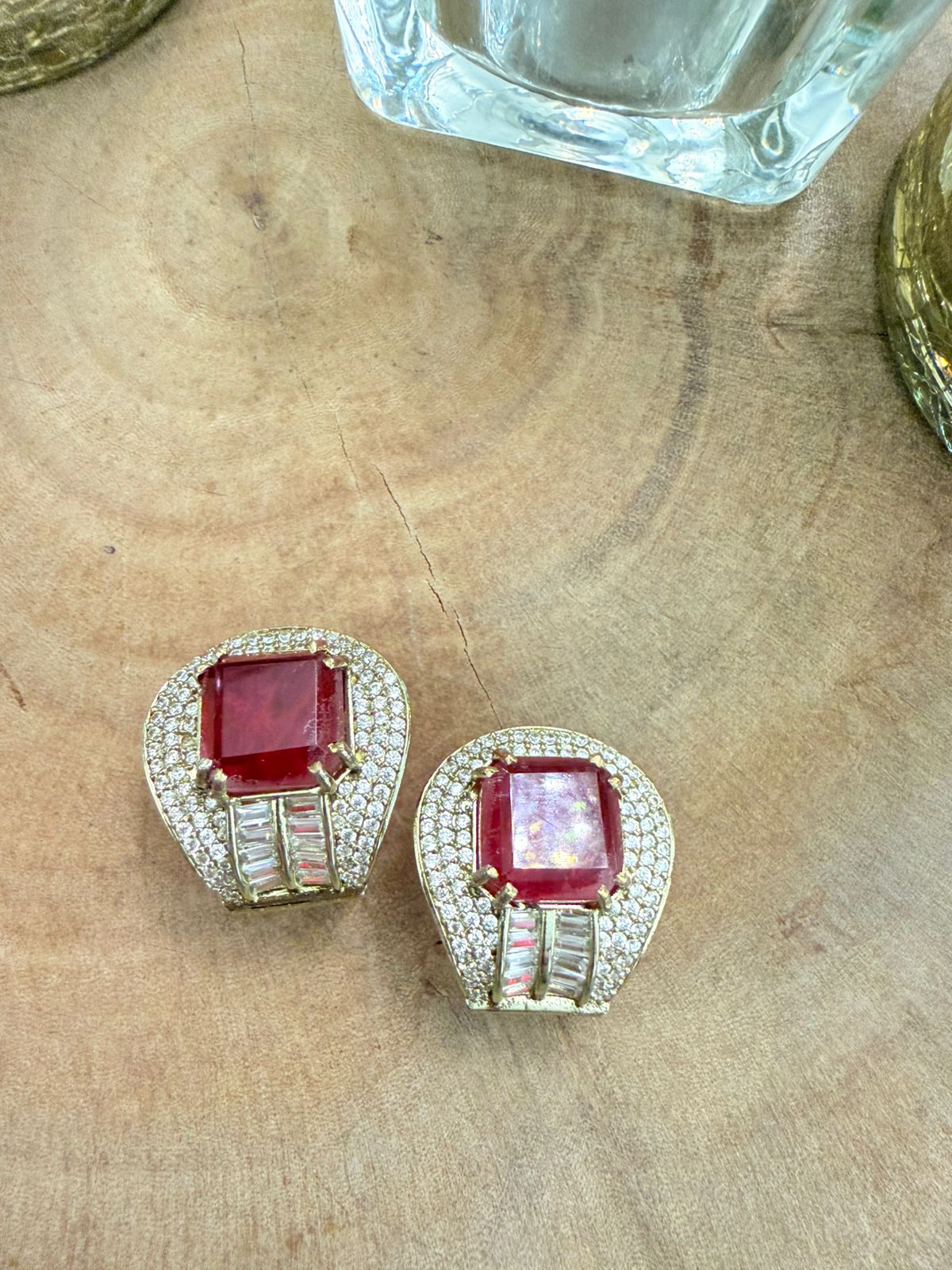 Pair of earrings with red gemstones and diamond accents on a wooden surface