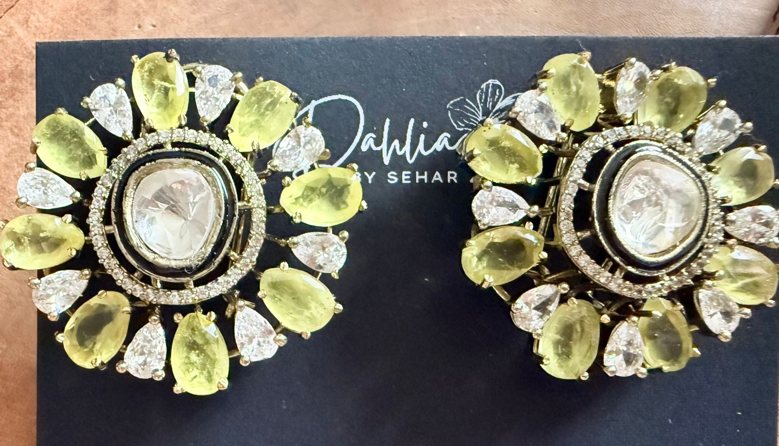 Pair of ornate earrings with green and gold stones on a black background with 'Dahlia by Sehar' branding.