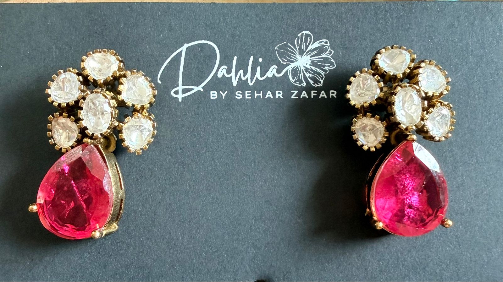 Pair of earrings with pink gemstones and gold accents on a dark background with 'Dahlia by Sehar Zafar' branding.