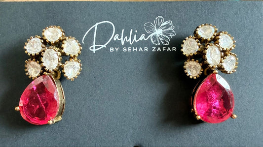 Pair of earrings with pink gemstones and gold accents on a dark background with 'Dahlia by Sehar Zafar' branding.