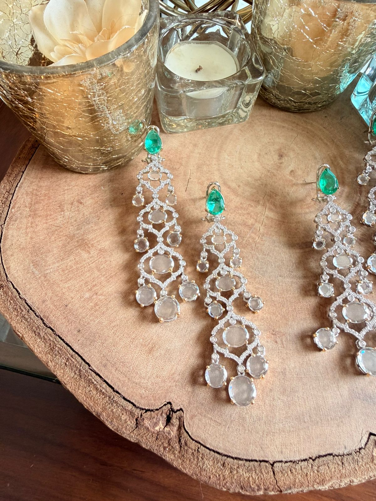 Pair of silver chandelier earrings with green gemstones on a wooden surface.