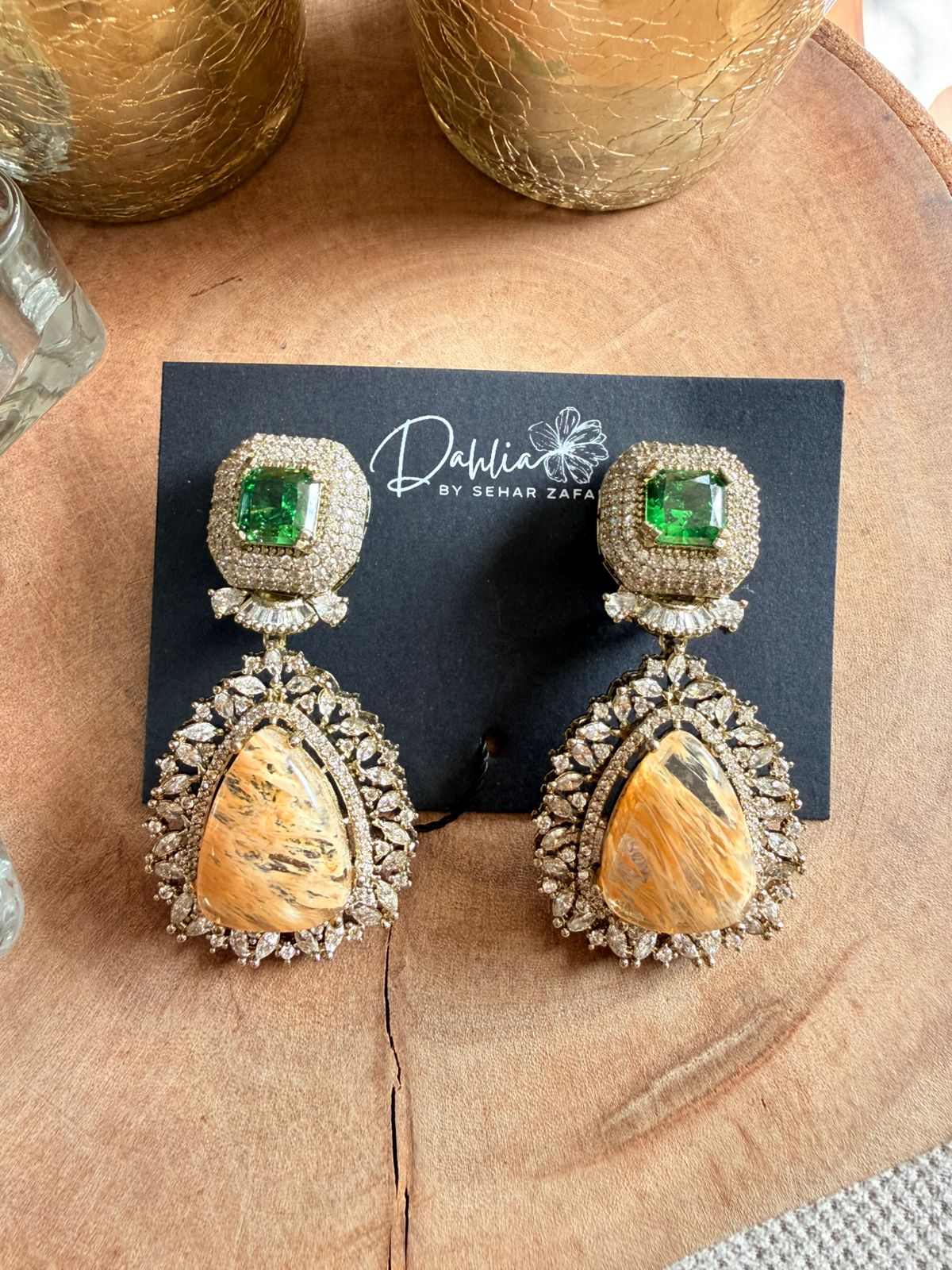 Pair of ornate earrings with gemstones on a branded card, placed on a wooden surface.